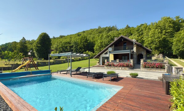 Ein Poolbereich mit Holzterrasse, Liegestühlen und einer Rutsche.