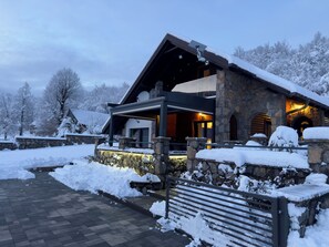 Ein Steinhaus mit geneigtem Dach, einem überdachten Eingang und verschneiter Landschaft.