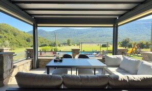Ein überdachter Außenbereich mit Tisch und Stühlen, mit Blick auf eine gebirgige Landschaft.
