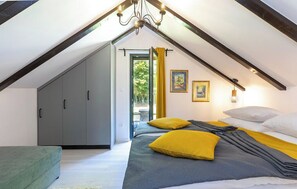 Ein Schlafzimmer mit schrägem Dach, einem Bett mit gelben Kissen, einem grauen Kleiderschrank und einer Chandelüster.
