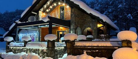 A snow-covered lodge with a stone facade, a large glass entrance, and a wooden roof.