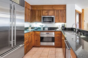 A kitchen with wooden cabinets, stainless steel appliances, a microwave, and a sink. - Austria Haus Club 2 bed 2 bath (Vail)