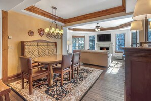 A dining area with a wooden table and chairs, a chandelier, and a fireplace in the background. - Austria Haus Club 2 bed 2 bath (Vail)