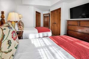 A hotel room with a bed, a dresser, a TV, and two doors. - Austria Haus Club 2 bed 2 bath (Vail)