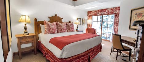 A bedroom with a large bed, wooden headboard, two bedside tables with lamps, a desk with a chair, and a window with curtains.