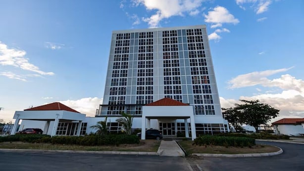 Un edificio de varios pisos con una entrada central y un estacionamiento al frente.