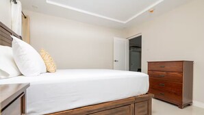 Un dormitorio con cama, cómoda de madera y puerta que da a otra habitación.