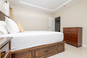 A bedroom with a bed, a wooden dresser, and a door leading to another room. - Modern 2BR 2BA Oasis in Portmore • Smart TV • AC • Free Parking (Portmore)