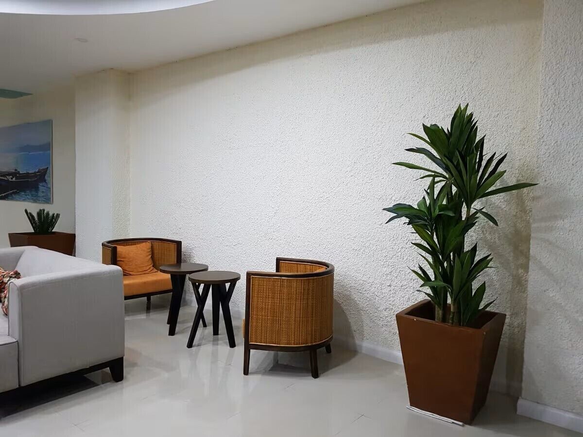 Uma sala de estar moderna com sofá, duas poltronas, mesa de centro e uma grande planta em vaso.