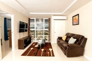 A modern living room with a leather sofa, a flat-screen TV, a dining table, and a large window with a city view.