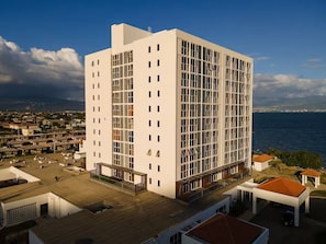 A modern multi-story building with a flat roof, large windows, and a view of the sea. - Modern 2BR 2BA Oasis in Portmore • Smart TV • AC • Free Parking (Portmore)
