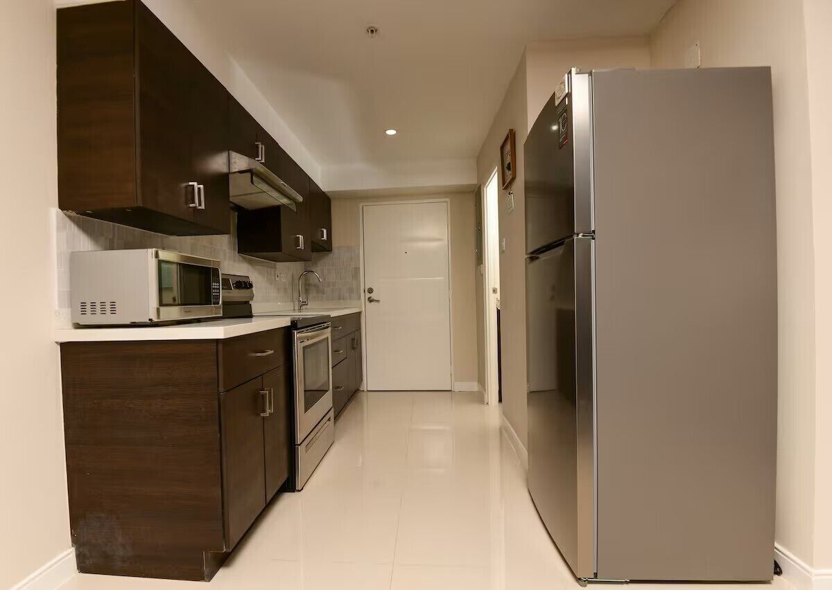 Cozinha moderna com eletrodomésticos de aço inoxidável, armários de madeira e piso de azulejos brancos.