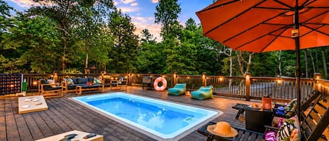 Une terrasse en bois avec un jacuzzi, des chaises longues et un parasol.