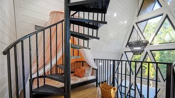 Un escalier en colimaçon avec une rampe noire menant à une chambre à coucher où se trouvent un lit et une fenêtre.