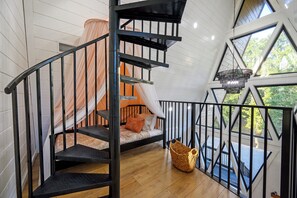 Eine Wendeltreppe mit schwarzer Geländer führt zu einem Schlafzimmer mit Bett und Fenster.