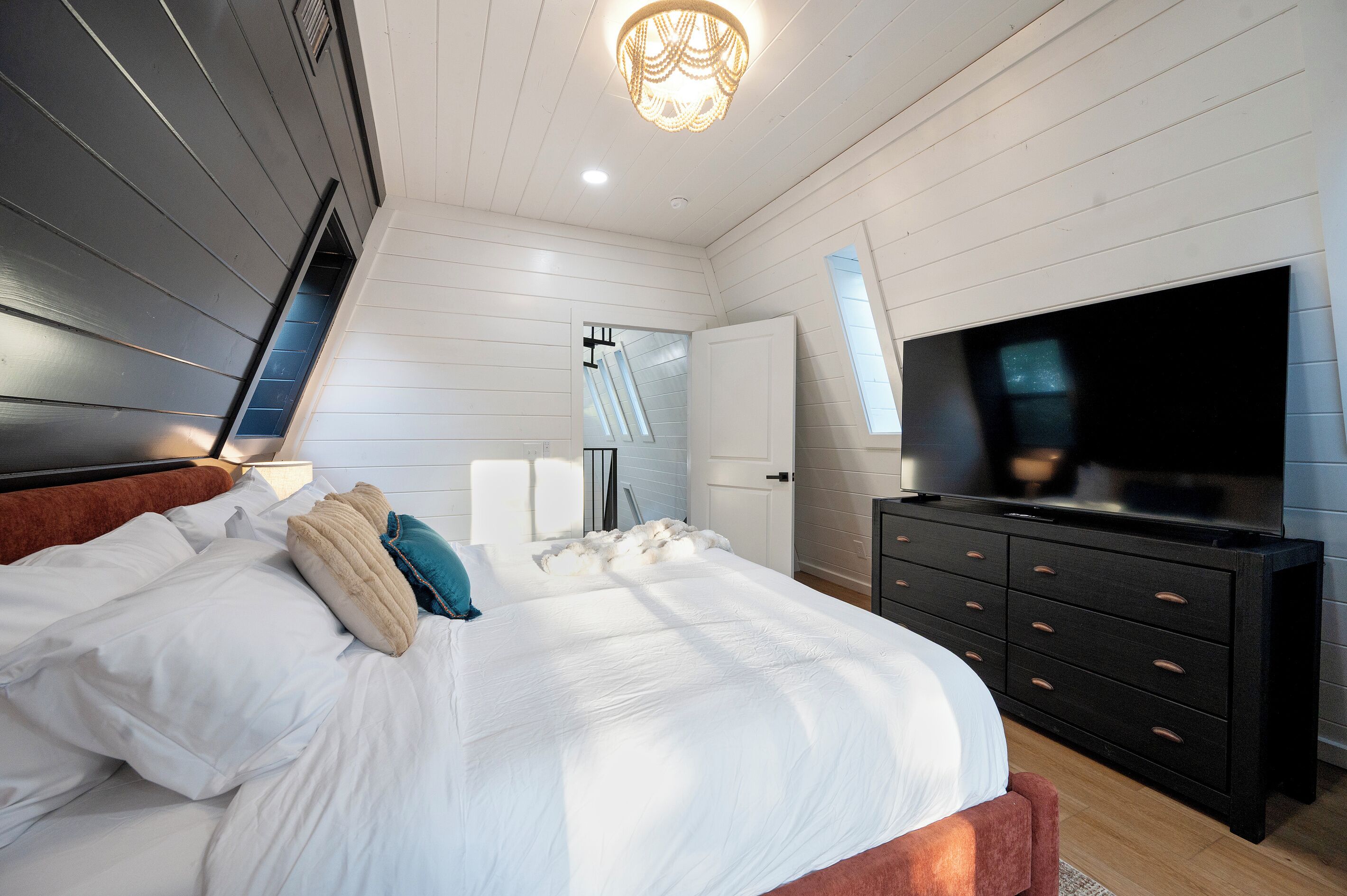 A bedroom with a bed, a dresser, a television, and a ceiling light.