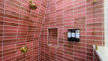 A bathroom with red-tiled walls, a showerhead, and a shelf with bottles of shampoo and conditioner.