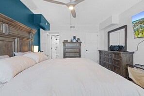 Ein Schlafzimmer mit einem großen Bett, einem Schminktisch, einem Spiegel und einem Deckenventilator.