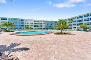 Ein Hotelpoolbereich mit einem runden Pool, Liegestühlen und Palmen.