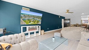 Ein modernes Wohnzimmer mit einem großen Flachbildfernseher, einem Glastisch und einem beigefarbenen Ecksofa.