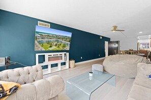 Ein modernes Wohnzimmer mit einem großen Flachbildfernseher, einem Glastisch und einem beigefarbenen Ecksofa.