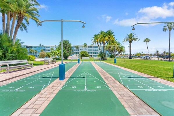 Ein Shuffleboardfeld mit grüner Spielfläche, umgeben von Palmen und einem wolkenlosen Himmel.