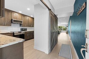 A modern kitchen with wooden cabinets, a stainless steel microwave, and a sliding door leading to a living area. - Salty Breeze Escape|Pool|GulfView (St. Pete Beach)