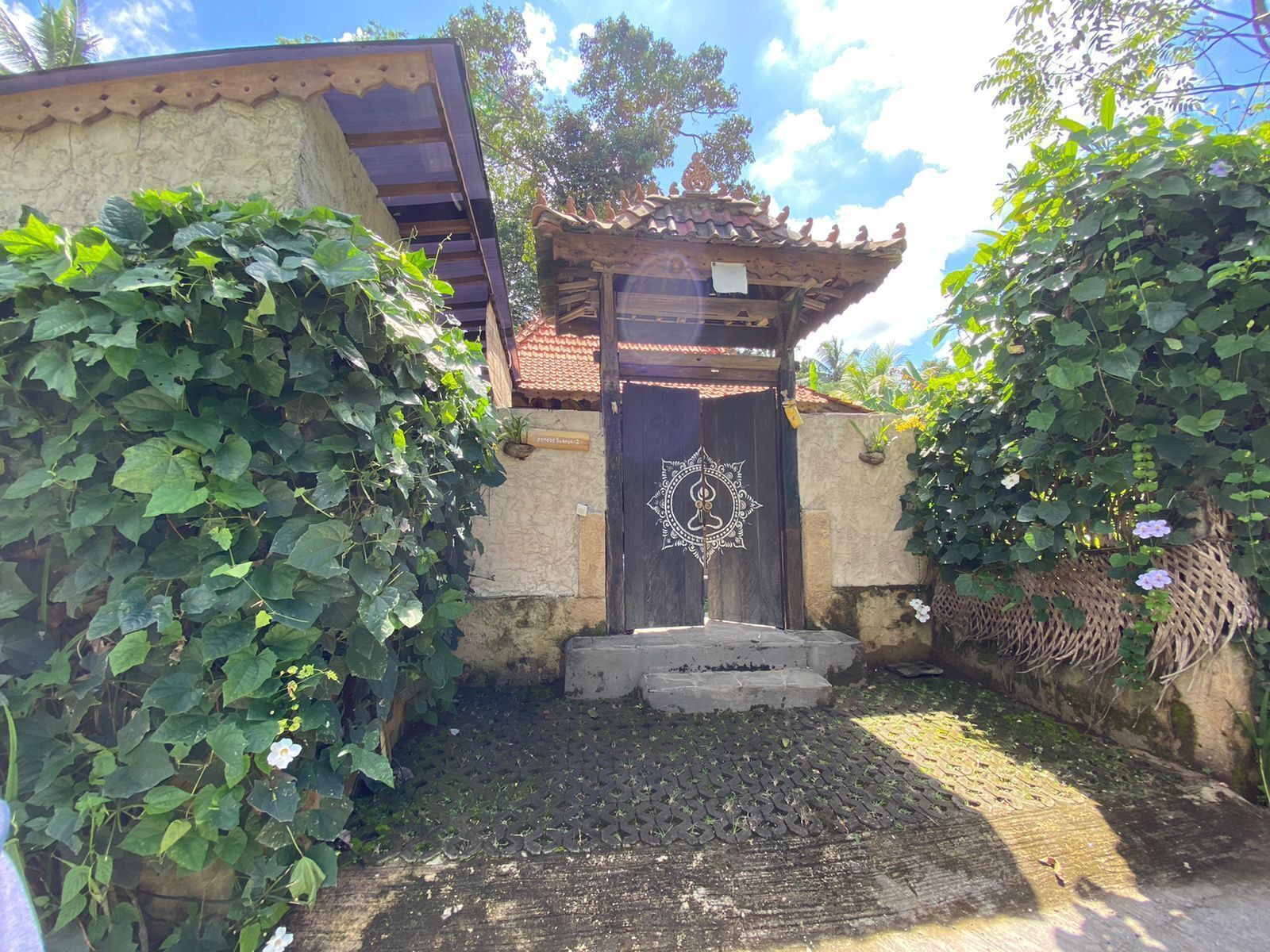 A traditional gate with a decorative emblem, surrounded by lush greenery and a stone wall.