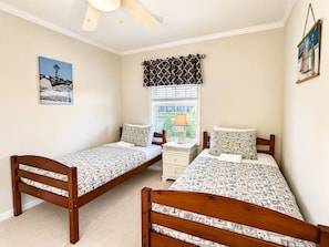 A bedroom with two single beds, a nightstand, a window with curtains, and a ceiling fan.
