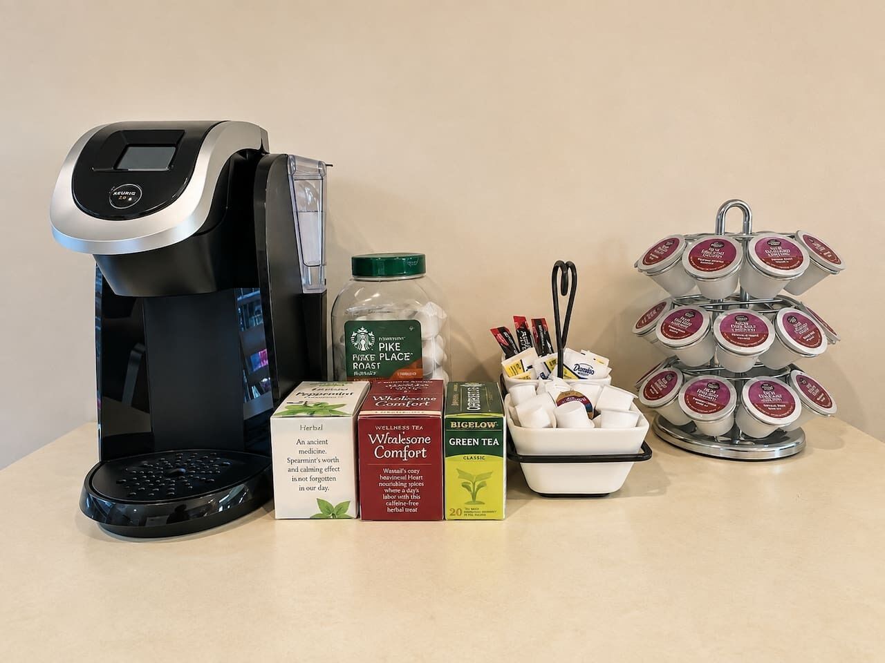 Eine Kaffeemaschine, ein Glas Pike Place Roast, Kisten mit Wellness-Tee, Bigelow Grüntee und ein Teeei mit Teebeuteln.