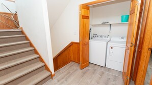 A laundry room with a washer and dryer, a wooden door, and a carpeted staircase. - Oceanside, close to beach, Priv. Pool, Hot Tub, Dogs Welcome-  WW1033, Driftwood I (Corolla)