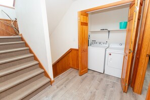 A laundry room with a washer and dryer, a wooden door, and a carpeted staircase. - Oceanside, close to beach, Priv. Pool, Hot Tub, Dogs Welcome-  WW1033, Driftwood I (Corolla)