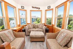 Una habitación con ventanas amplias, un conjunto de sofás, una pequeña mesa y un adorno en la pared.