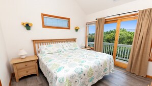 A bedroom with a bed, a nightstand, a window with curtains, and a view of greenery outside. - Oceanside, close to beach, Priv. Pool, Hot Tub, Dogs Welcome-  WW1033, Driftwood I (Corolla)