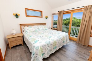 A bedroom with a bed, a nightstand, a window with curtains, and a view of greenery outside. - Oceanside, close to beach, Priv. Pool, Hot Tub, Dogs Welcome-  WW1033, Driftwood I (Corolla)