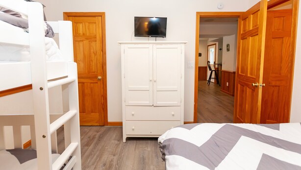A bedroom with bunk beds, a wardrobe, a television, and wooden doors. - Oceanside, close to beach, Priv. Pool, Hot Tub, Dogs Welcome-  WW1033, Driftwood I (Corolla)
