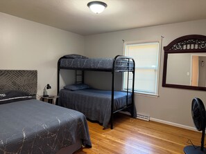 A room with a bunk bed, a desk with a lamp, a mirror, and a standing fan. - Hakuna Matata #6: Home for 12 People - 12 Minutes from Fort Bragg (Fayetteville)
