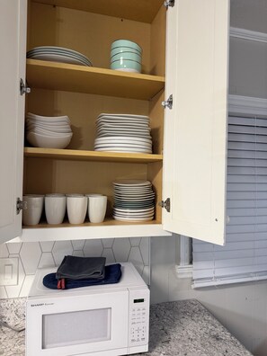 A kitchen with a microwave, cabinets with dishes, and a window with blinds. - Hakuna Matata #6: Home for 12 People - 12 Minutes from Fort Bragg (Fayetteville)