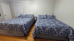 Een slaapkamer met twee bedden, een plafondventilator, een raam met jaloezieën en een deur.