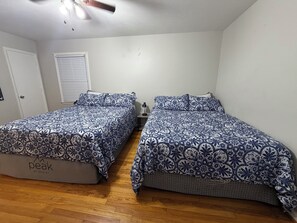 A bedroom with two beds, a ceiling fan, a window with blinds, and a door. - Hakuna Matata #6: Home for 12 People - 12 Minutes from Fort Bragg (Fayetteville)