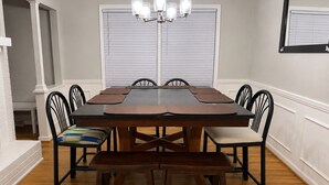Een eetkamer met een rechthoekige tafel, zes stoelen, een bank en een kroonluchter.