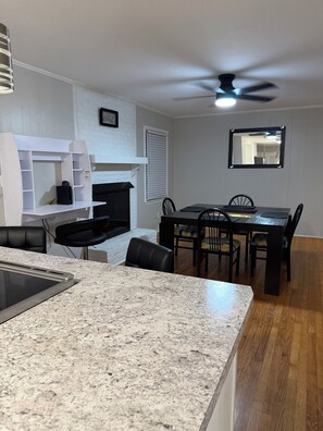 A modern kitchen with granite countertops, a dining area with a dark wooden table and chairs, and a ceiling fan. - Hakuna Matata #6: Home for 12 People - 12 Minutes from Fort Bragg (Fayetteville)