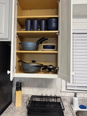 A kitchen with wooden shelves holding cookware, a knife block, and a dish rack. - Hakuna Matata #6: Home for 12 People - 12 Minutes from Fort Bragg (Fayetteville)