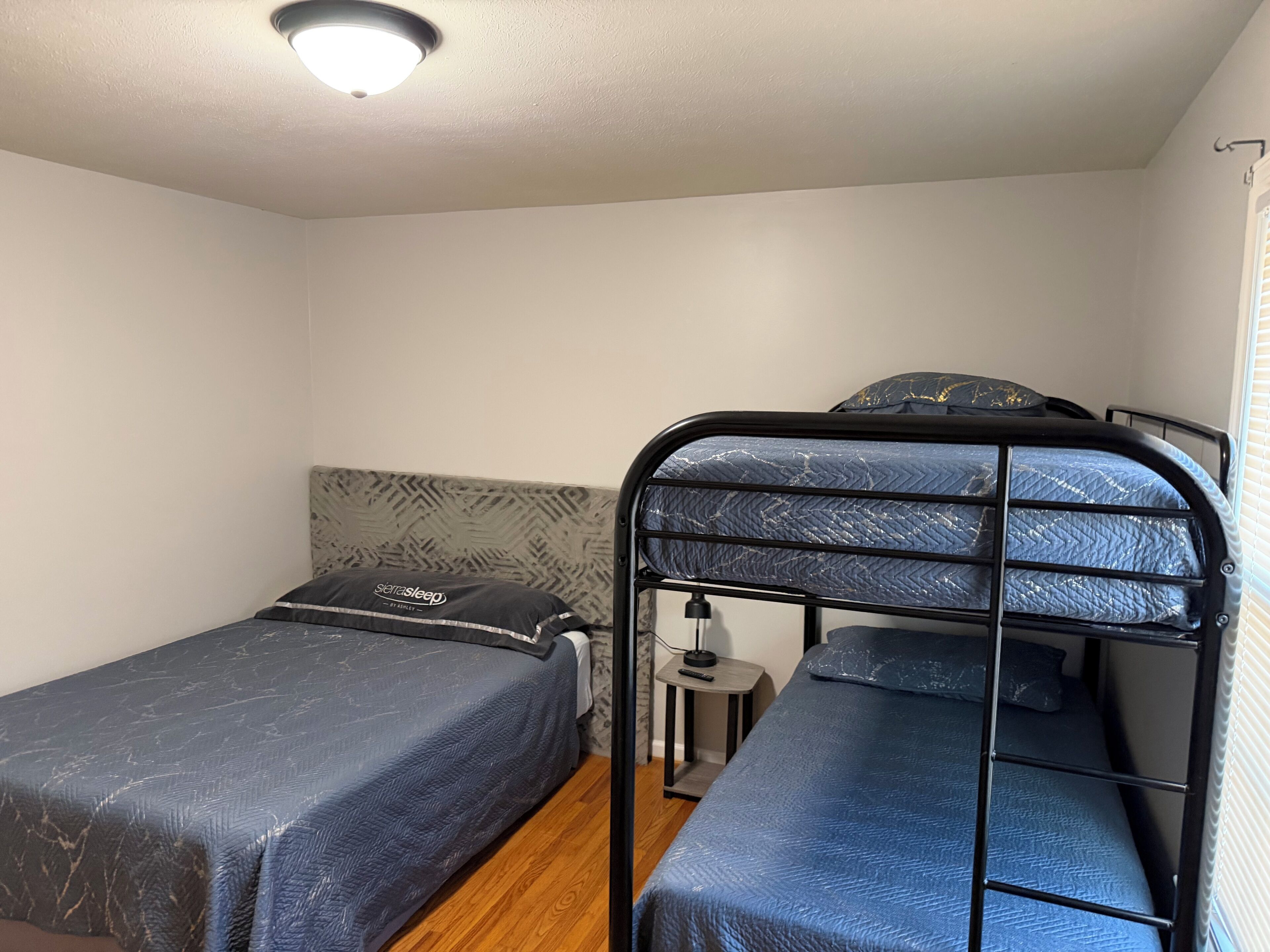 A small, single-room accommodation with two bunk beds, a bedside table with a lamp, and a ceiling light fixture.
