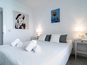 A hotel room with a bed, two bedside tables, a wall with artwork, and rolled towels on the bed. - Naricha 3 Apartments by Casasol by Interhome (Nerja)