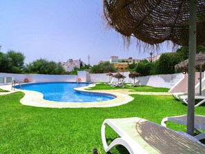A swimming pool with a surrounding grassy area, lounge chairs, and a thatched umbrella. - Naricha 3 Apartments by Casasol by Interhome (Nerja)