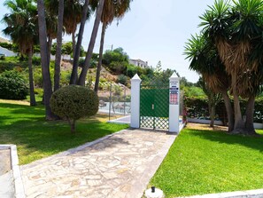 A gated entrance with a stone pathway leading to a building, surrounded by palm trees and greenery. - Naricha 3 Apartments by Casasol by Interhome (Nerja)