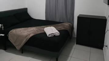 Un dormitorio con cama, mesita de noche, televisor de pantalla plana y ventana con cortinas.