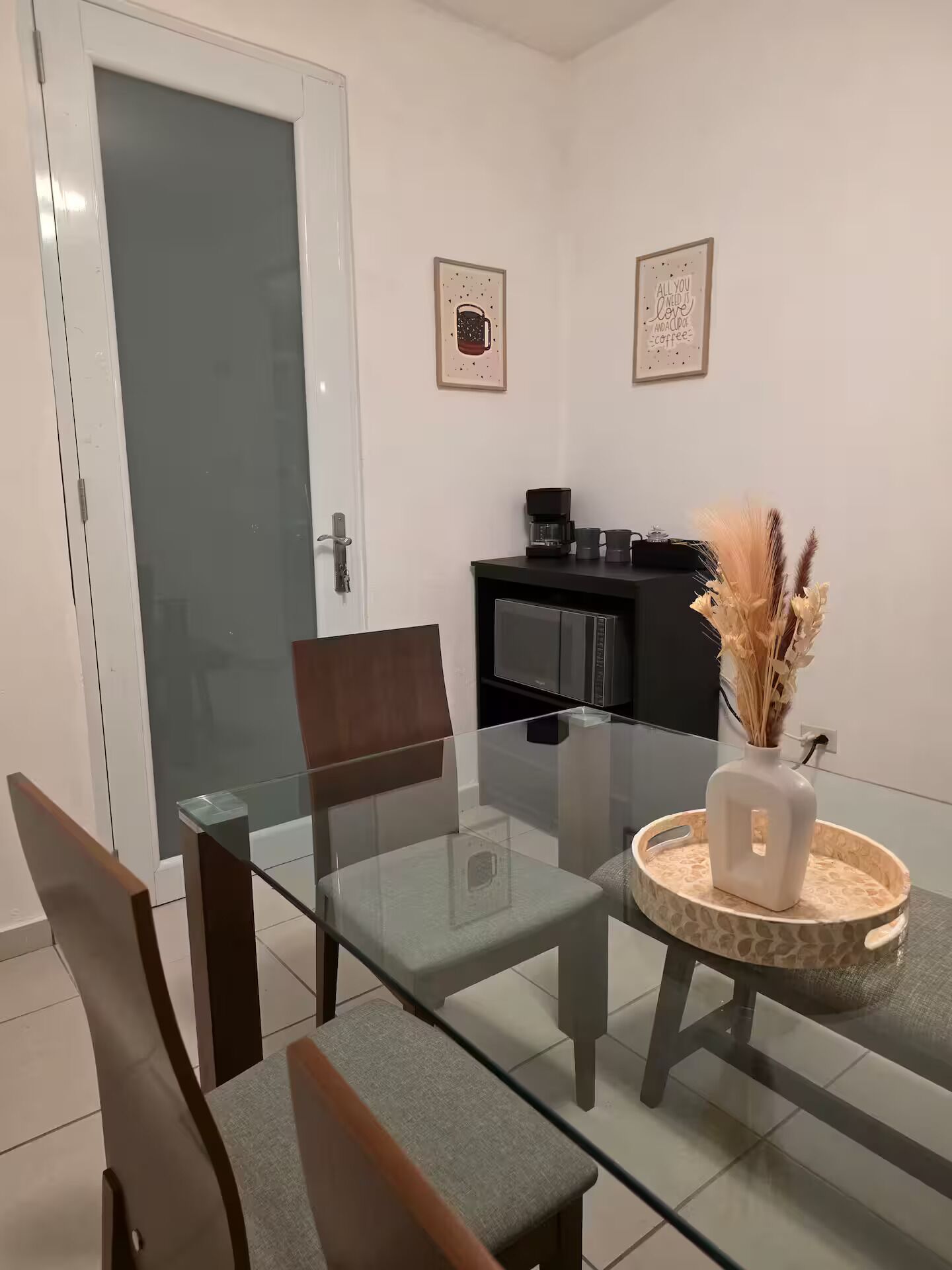 A modern dining area with a glass table, two chairs, a coffee machine, and decorative wall art.
