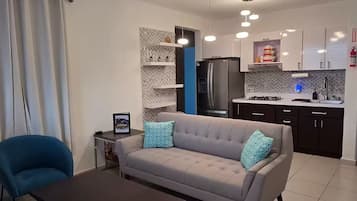 Una sala de estar moderna con un sofá, una mesa de centro y una cocina al fondo.